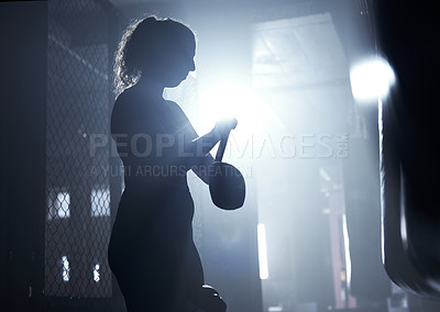 Buy stock photo Shot of a sporty young woman strapping her gloves while boxing in a gym