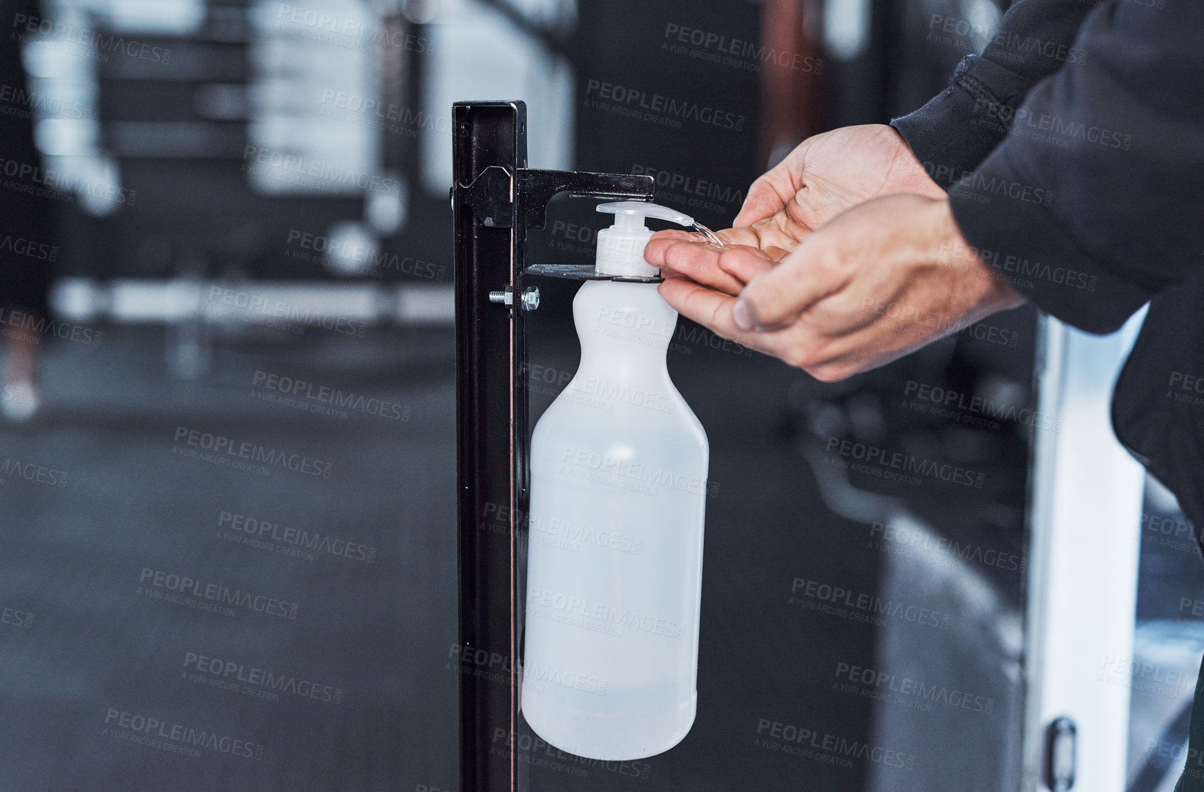 Buy stock photo Closeup shot of an unrecognisable man using a hand sanitiser dispenser in a gym