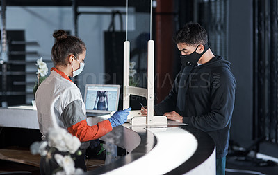 Buy stock photo Shot of a young man filling in paperwork at the reception desk of a gym