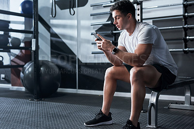 Buy stock photo Shot of a sporty young man using a cellphone in a gym