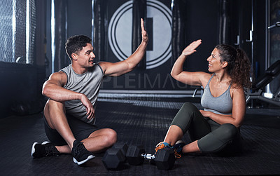 Buy stock photo Shot of two sporty young people giving each other a high five while exercising together in a gym