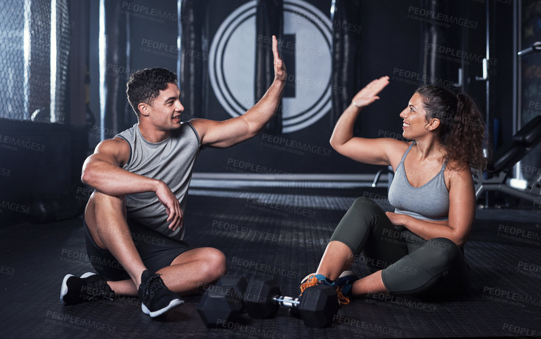 Buy stock photo Shot of two sporty young people giving each other a high five while exercising together in a gym