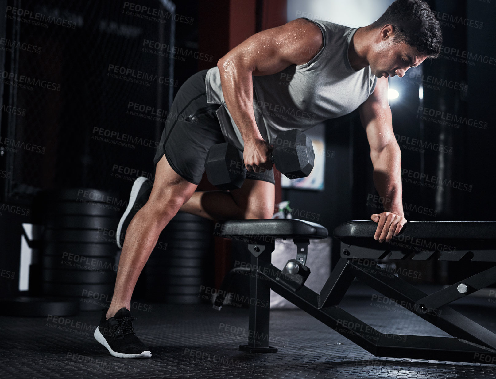Buy stock photo Shot of a muscular young man exercising with a dumbbell in a gym