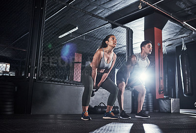 Buy stock photo Shot of two sporty young people exercising with kettlebells in a gym