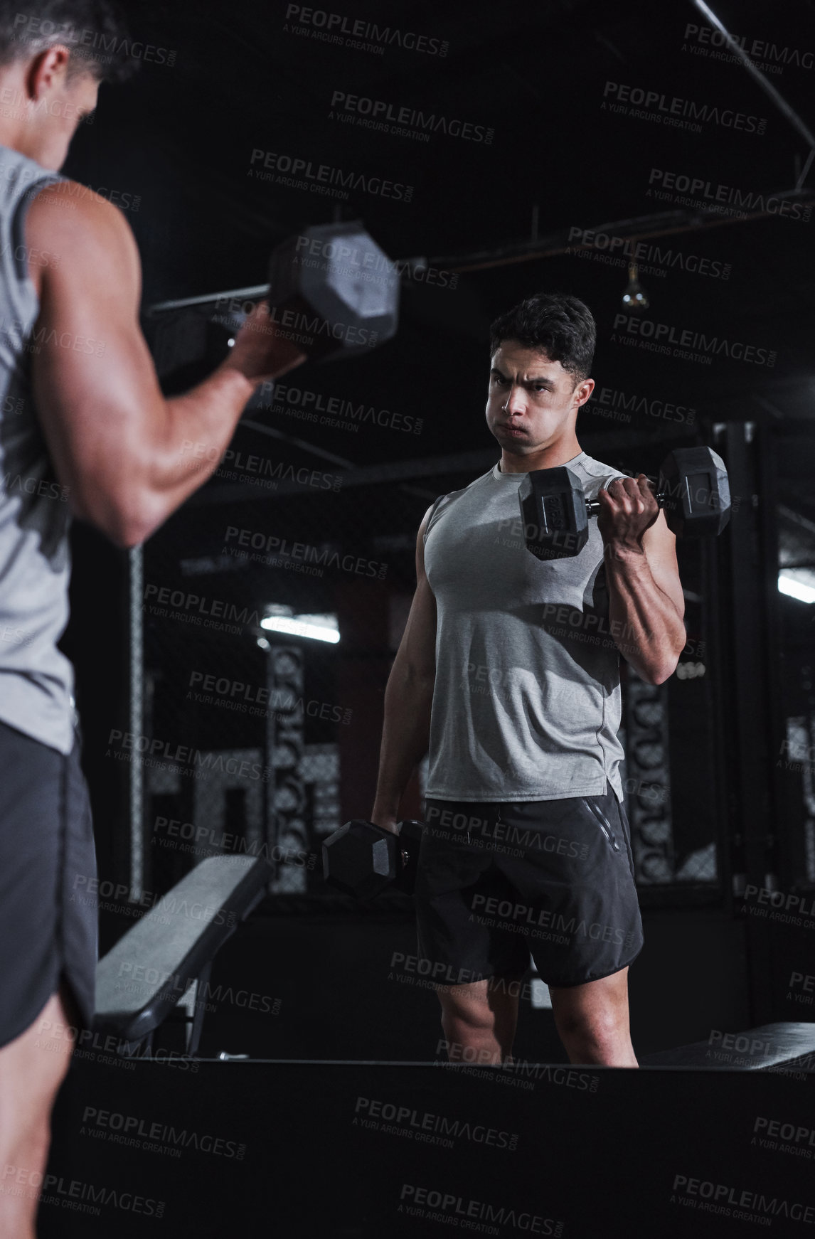 Buy stock photo Cropped shot of a handsome and athletic young man working out with dumbbells in the gym