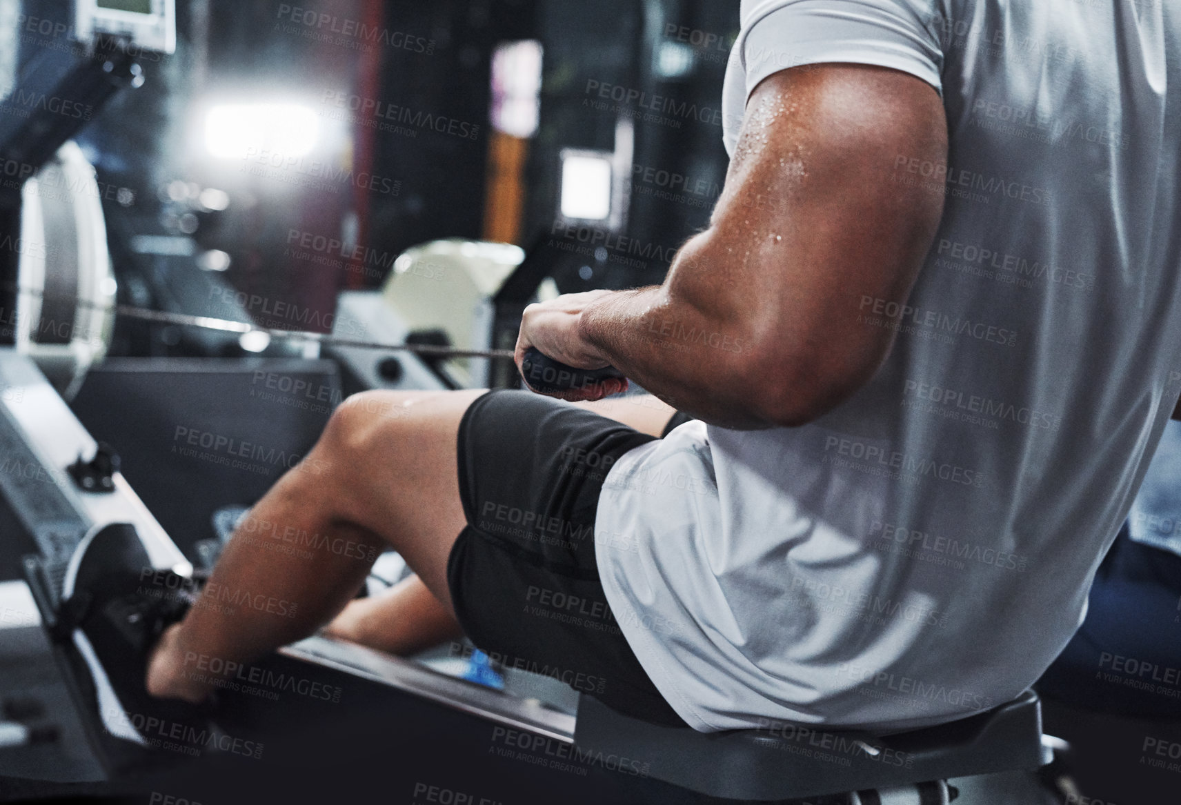 Buy stock photo Cropped shot of an unrecognizable male athlete working out on a rowing machine in the gym