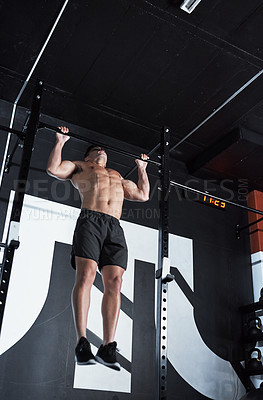 Buy stock photo Shot of a young man lifting doing pull ups at a gym