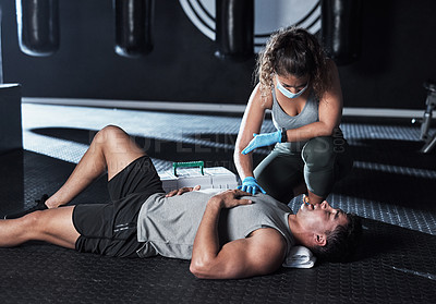 Buy stock photo Shot of a masked young woman giving an injured man first aid at the gym