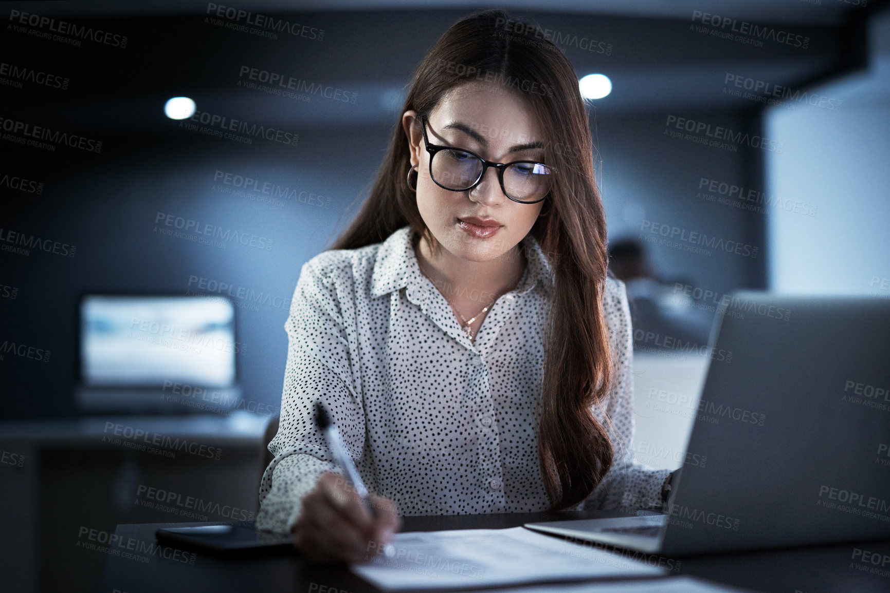 Buy stock photo Shot of a young businesswoman going through paperwork while working in an office at night