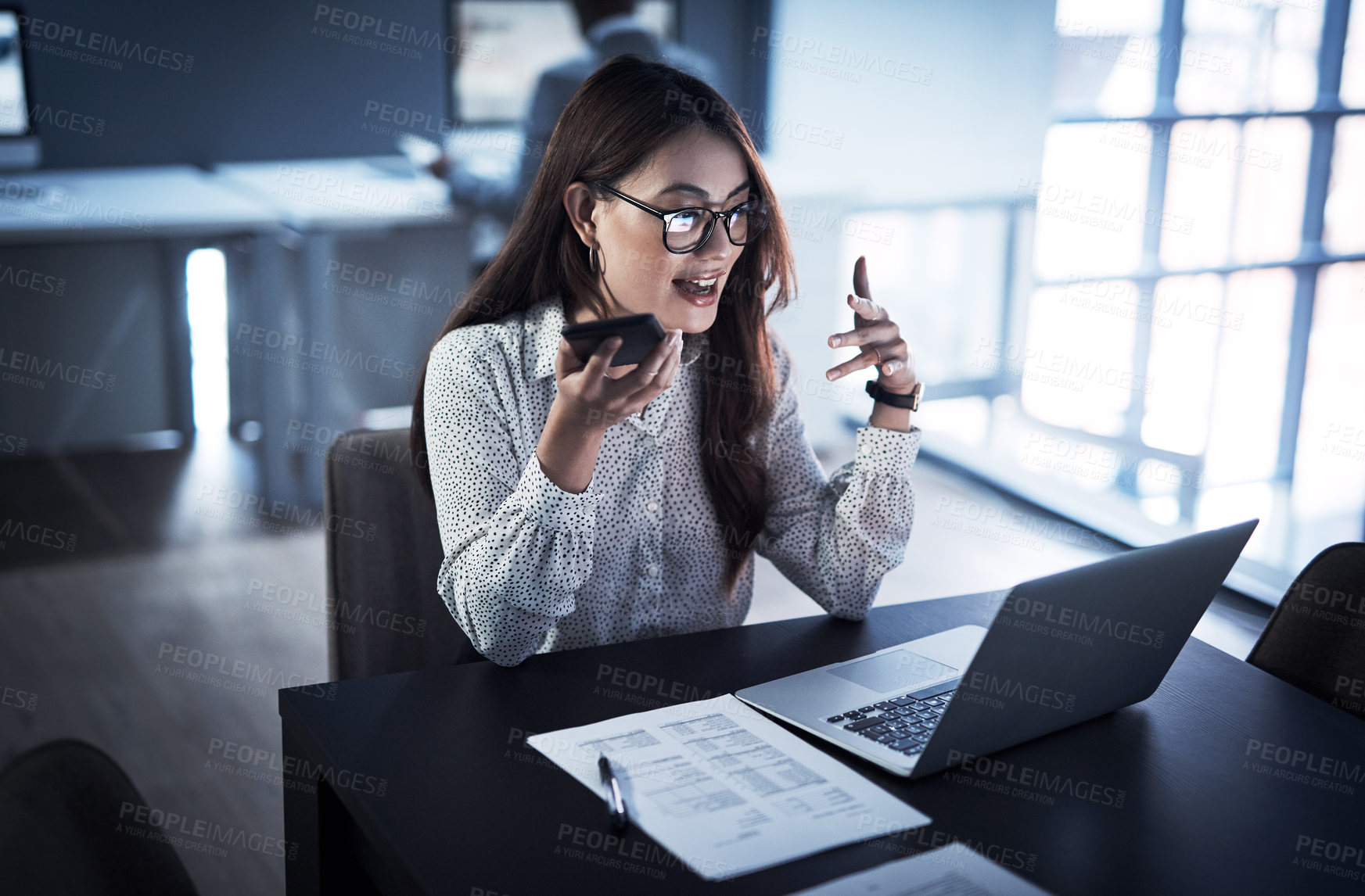 Buy stock photo Shot of a young businesswoman using a cellphone and laptop while working in an office at night