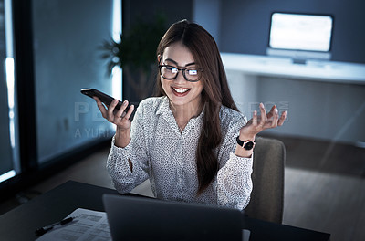 Buy stock photo Shot of a young businesswoman using a cellphone and laptop while working in an office at night