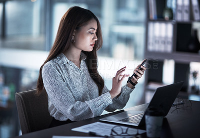 Buy stock photo Shot of a young businesswoman using a cellphone while working in an office at night