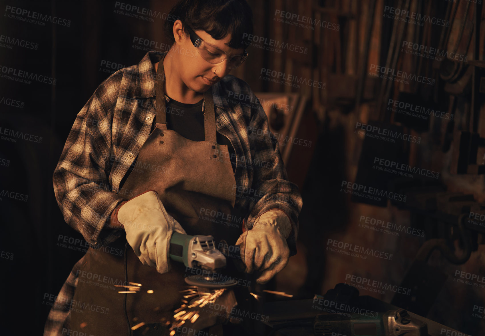 Buy stock photo Shot of a young woman using an angle grinder while working at a foundry