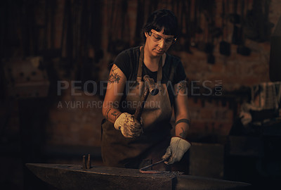Buy stock photo Shot of a young woman hitting a hot metal rod with a hammer in a foundry