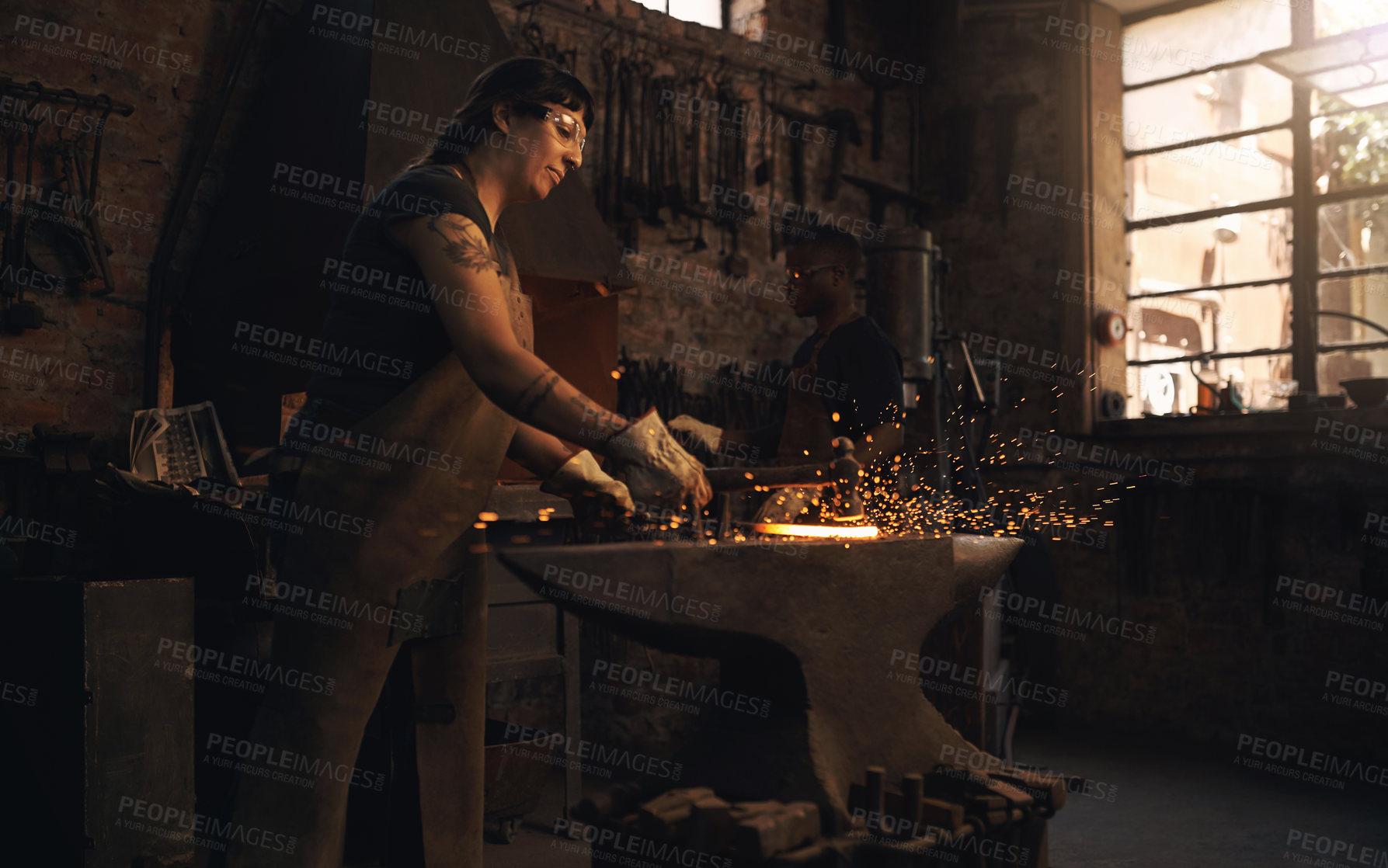Buy stock photo Shot of a young woman hitting a hot metal rod with a hammer in a foundry