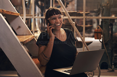 Buy stock photo Shot of a young woman using a laptop and smartphone while working at a foundry