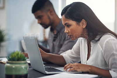 Buy stock photo Shot of a young businesswoman working on a laptop in an office with her colleague in the background