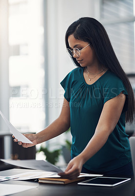 Buy stock photo Shot of a young businesswoman going through paperwork in an office