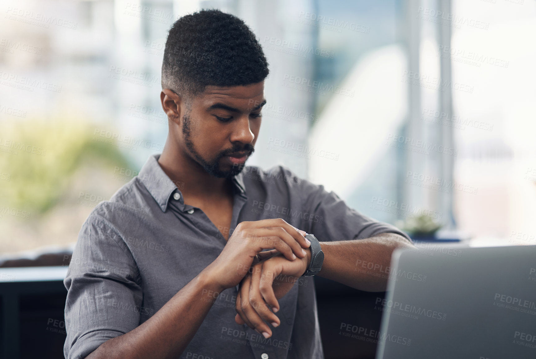 Buy stock photo Shot of a young businessman checking the time while working on a laptop in an office
