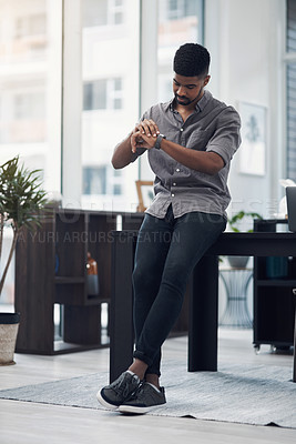 Buy stock photo Shot of a young businessman checking the time on his wristwatch in an office