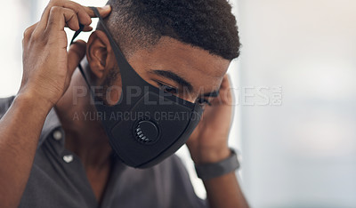 Buy stock photo Shot of a young businessman putting on a face mask in an office