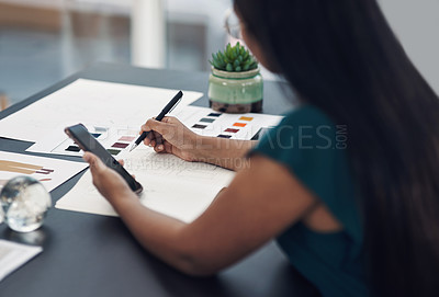 Buy stock photo Shot of a young designer writing notes while using a cellphone in an office