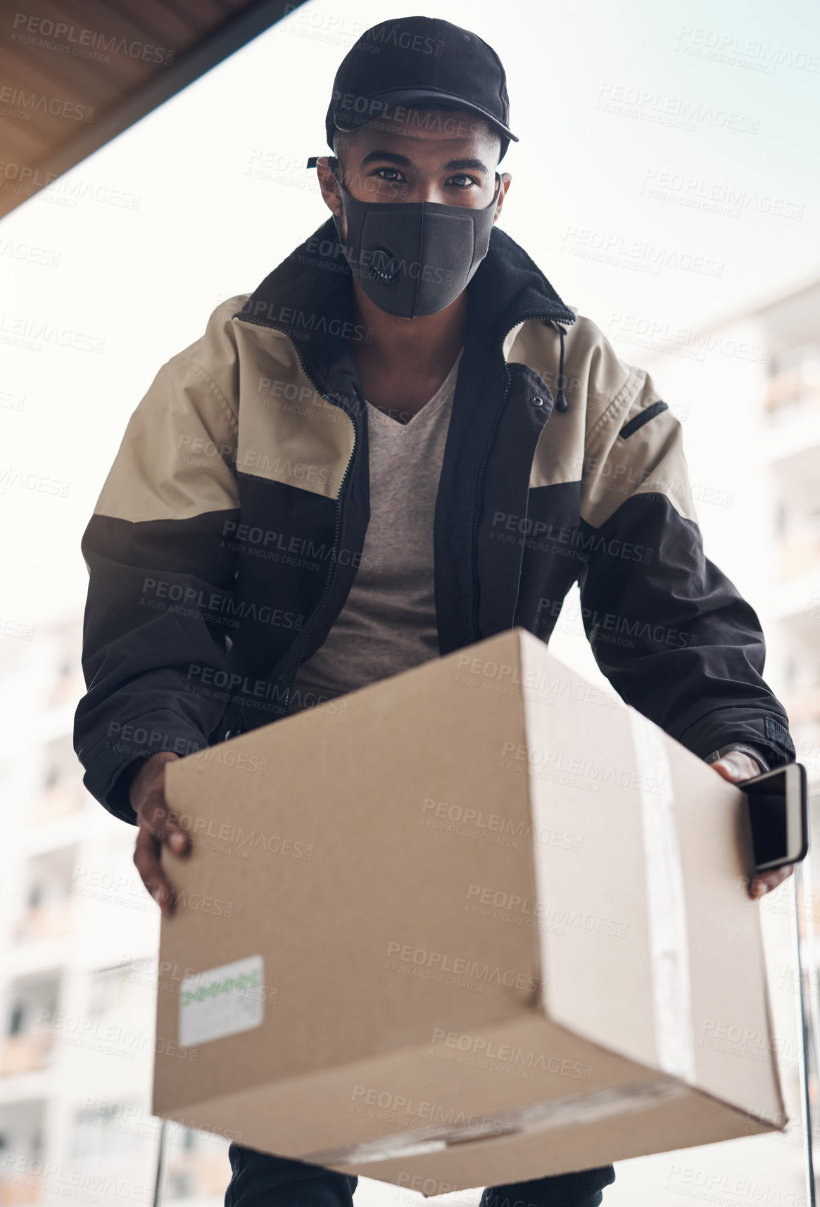 Buy stock photo Shot of a masked young man delivering a package to a place of residence