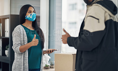 Buy stock photo Shot of a masked young woman showing thumbs up while receiving a delivery at home