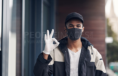 Buy stock photo Shot of a masked and gloved young man showing an okay sign while making a home delivery