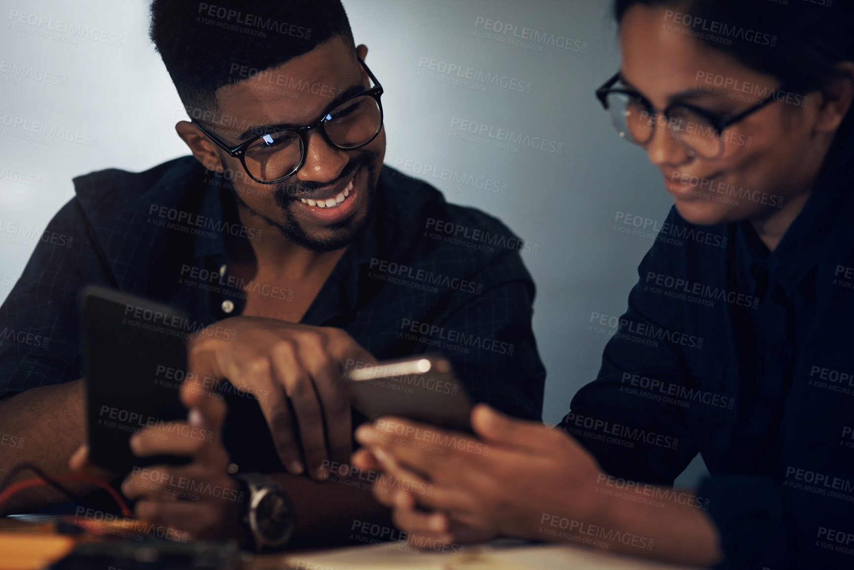Buy stock photo Shot of two young technicians using their smartphone while repairing computer hardware