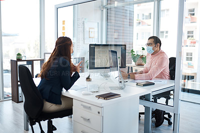 Buy stock photo Shot of two businesspeople wearing face masks while working together in an office