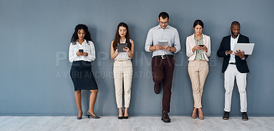 Buy stock photo Shot of a group of businesspeople using digital devices while standing in line against a grey background