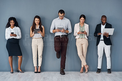 Buy stock photo Shot of a group of businesspeople using digital devices while standing in line against a grey background