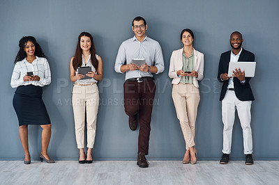 Buy stock photo Portrait of a group of businesspeople using digital devices while standing in line against a grey background