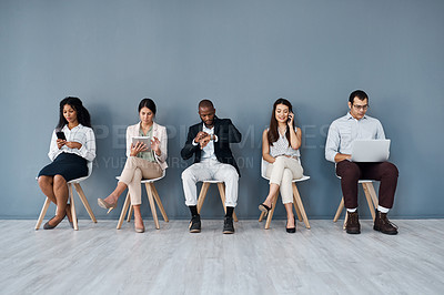 Buy stock photo Shot of a group of businesspeople using digital devices while sitting in line against a grey background