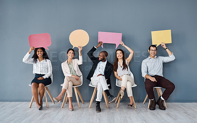 Buy stock photo Portrait of a group of businesspeople holding speech bubbles while sitting in line against a grey background