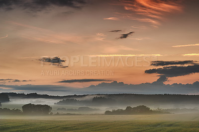 Buy stock photo Beautiful sunrise with mist against a dramatic and colorful sky background. Calm and breathtaking landscape view on a field in the countryside with blooming trees on a foggy and overcast morning 