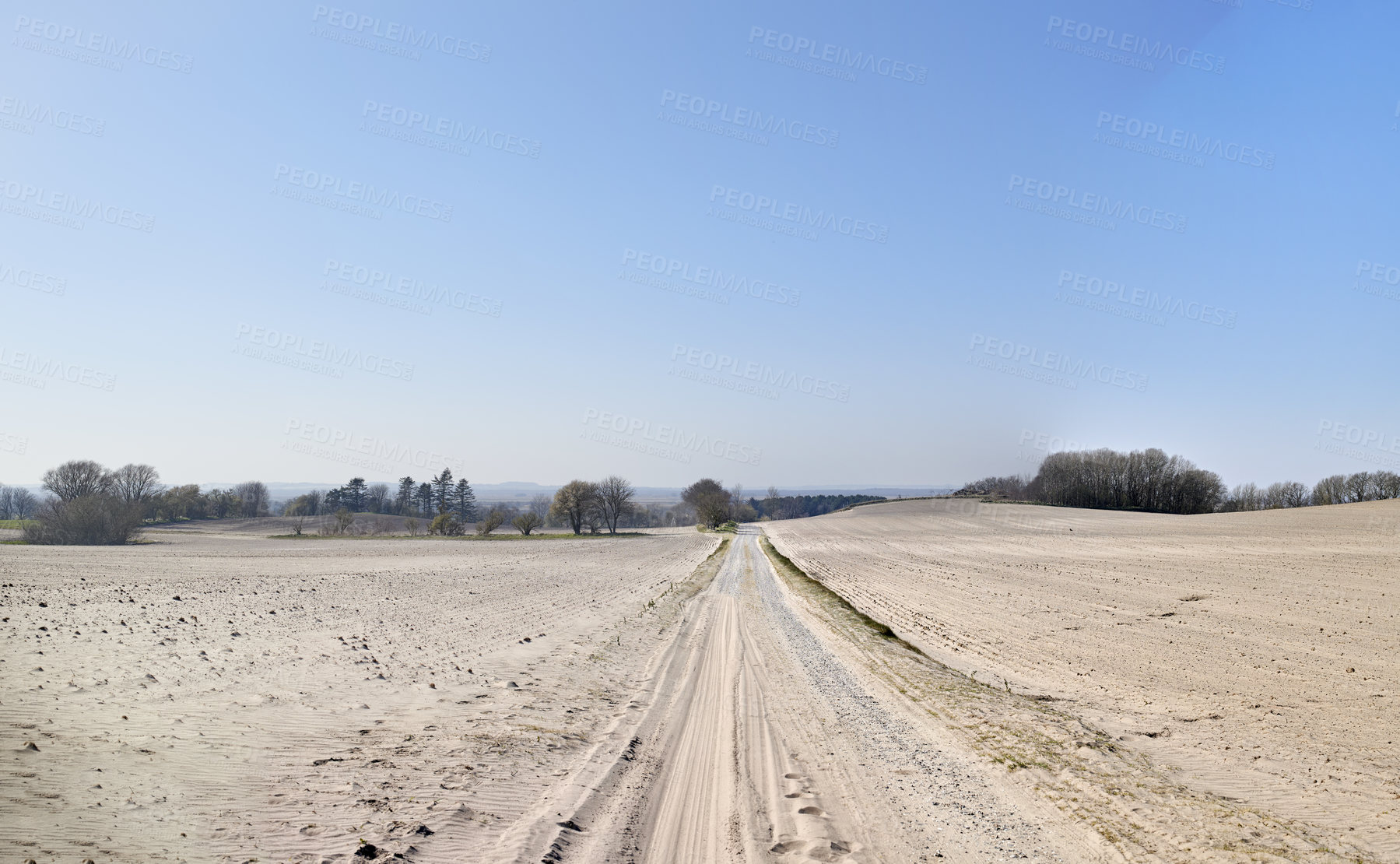 Buy stock photo A desolate agricultural farmland caused by summer heat droughts and impact on agriculture industry. Open and empty dry sand. Sandy and barren land with trees in the distance and blue sky background.