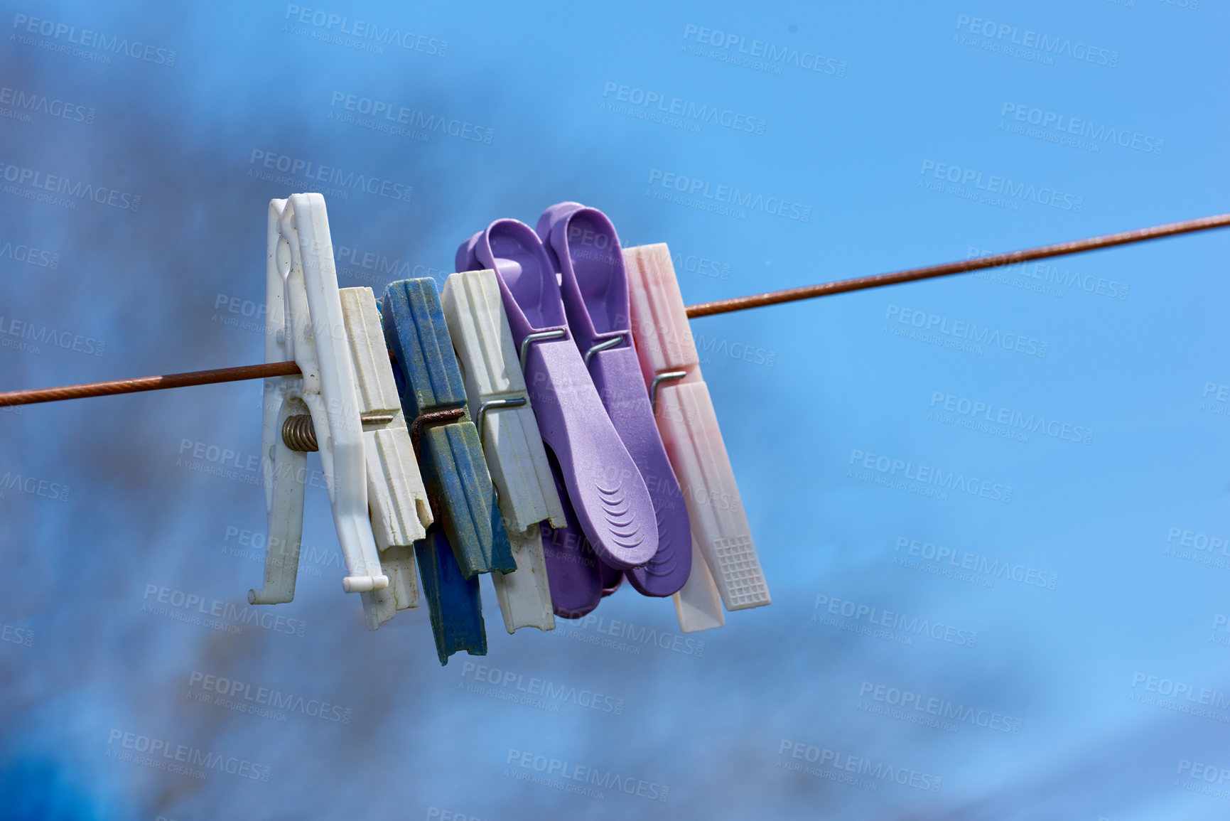 Buy stock photo Old washing line with broken pins hanging outside against a blurred blue background. Brown clothesline with different plastic pegs in a backyard on laundry day with copy space for domestic chores