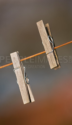 Buy stock photo Closeup of two clothing pegs on a washing line outside against a blurred background. Wooden clothespins used to clip and hang clean laundry in the sun to dry as part of household and domestic chores