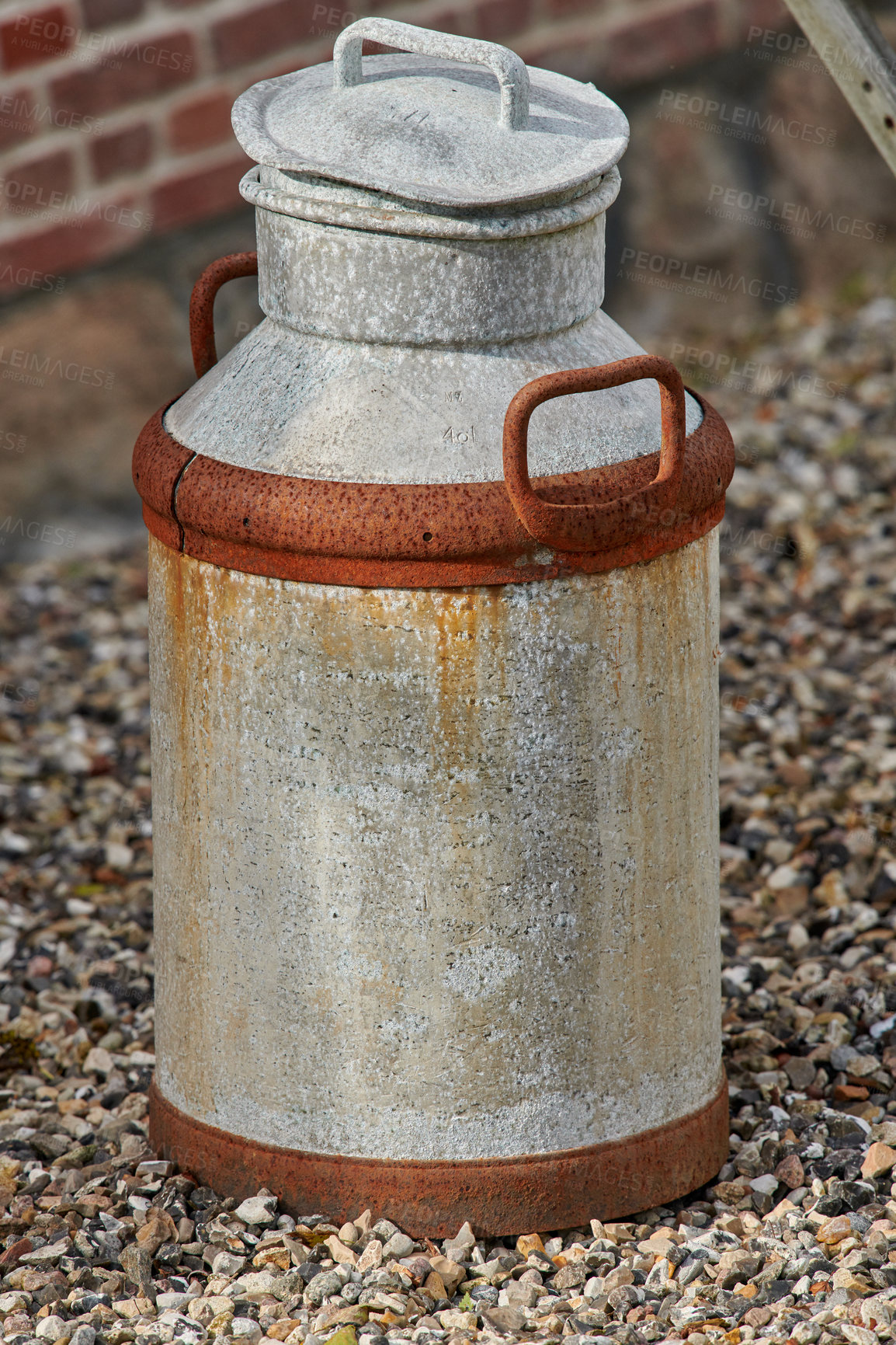 Buy stock photo An old rusted metal milk can on the ground from above. An antique dairy canister outside on a pebble covered walkway. A rusty and used metallic jug during the day with copy space 