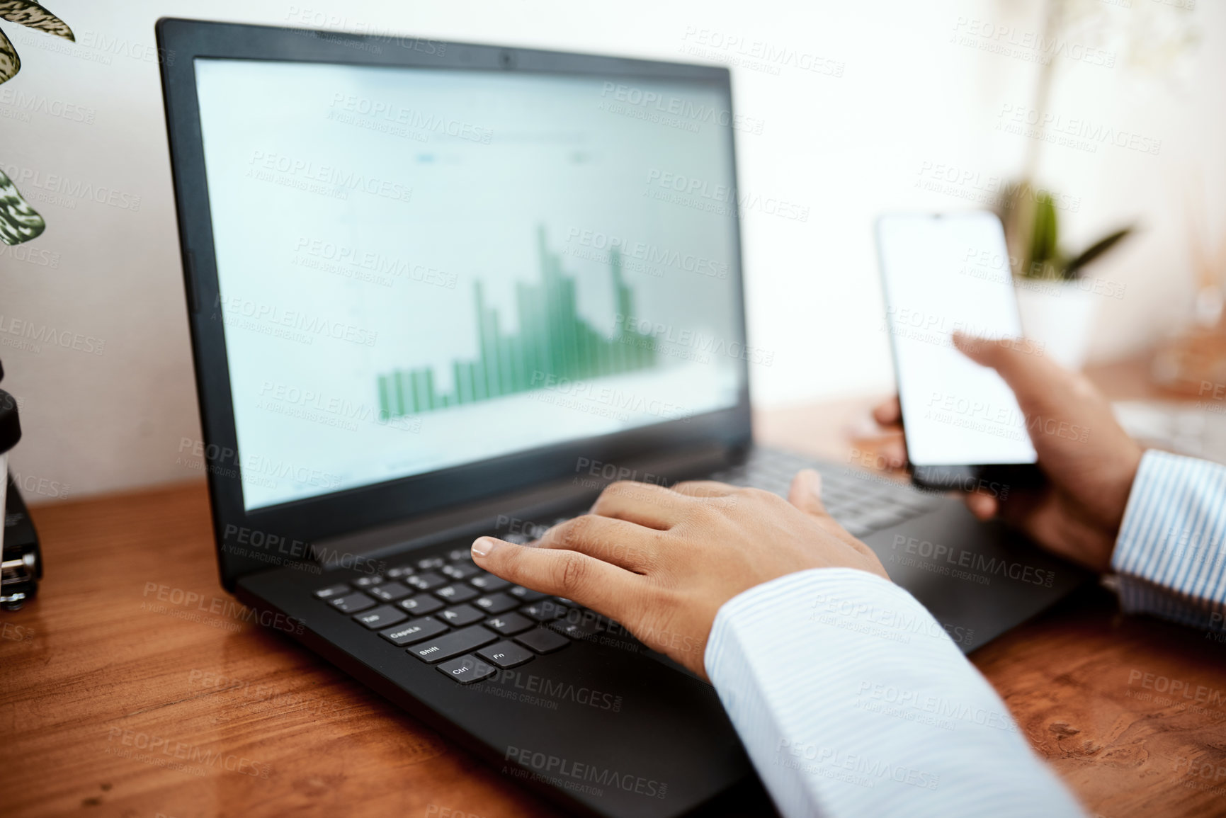 Buy stock photo Cropped shot of a businesswoman using a laptop and smartphone while analysing financial data at her desk