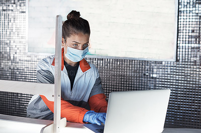 Buy stock photo Shot of a young woman wearing a face mask and using a laptop while working in a gym