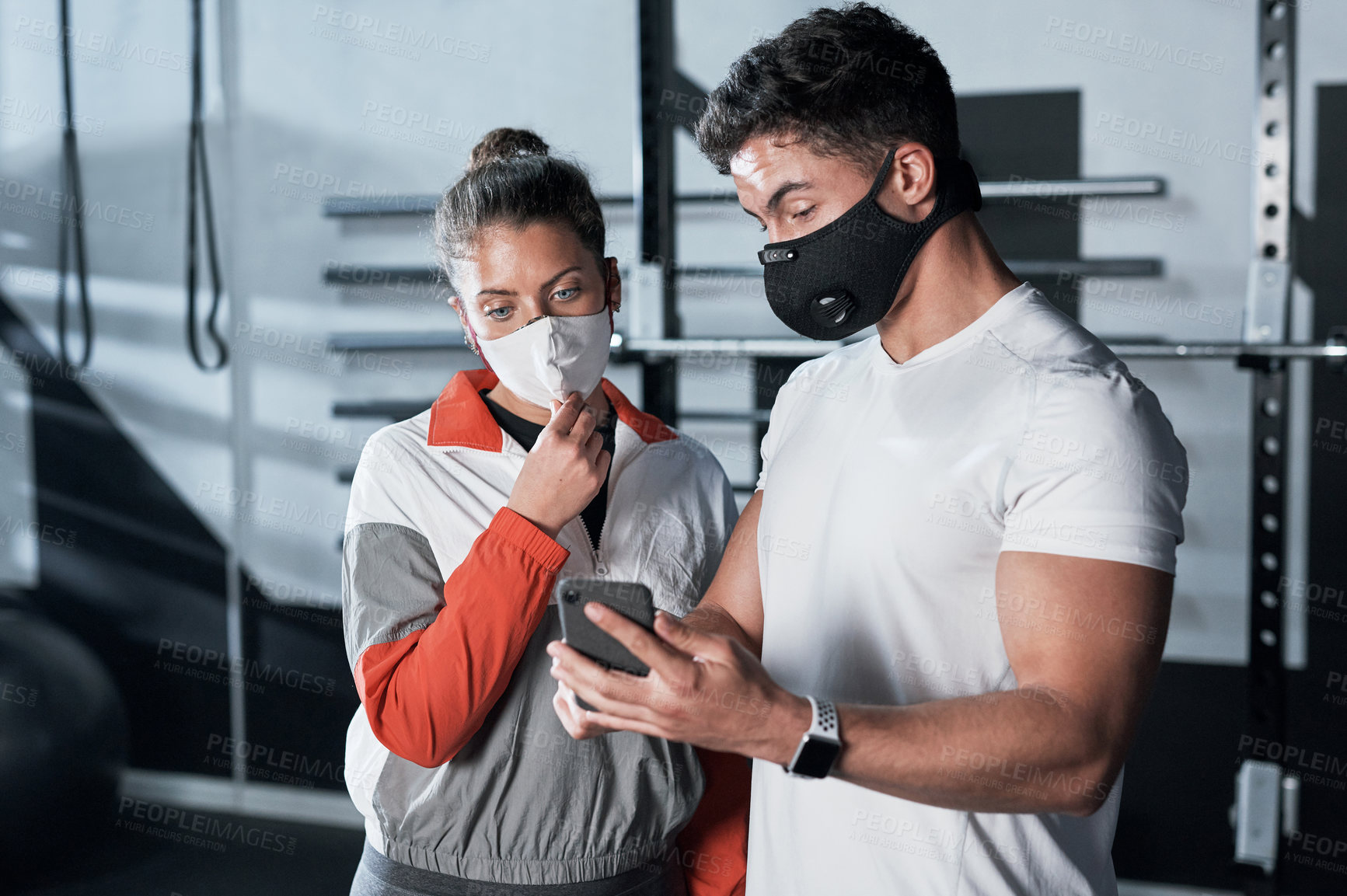 Buy stock photo Shot of two sporty people looking at something on a cellphone together in a gym