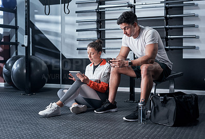 Buy stock photo Shot of two sporty young people using digital devices in a gym