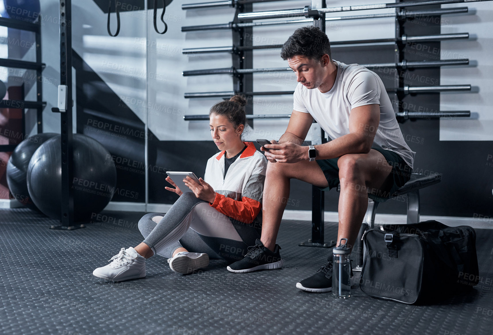 Buy stock photo Shot of two sporty young people using digital devices in a gym
