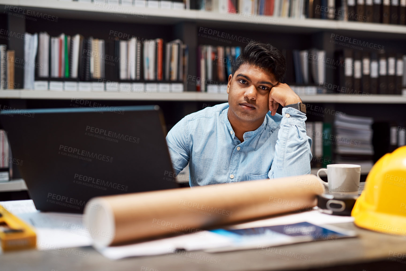 Buy stock photo Portrait of a young architect looking bored while working at his desk in a modern office