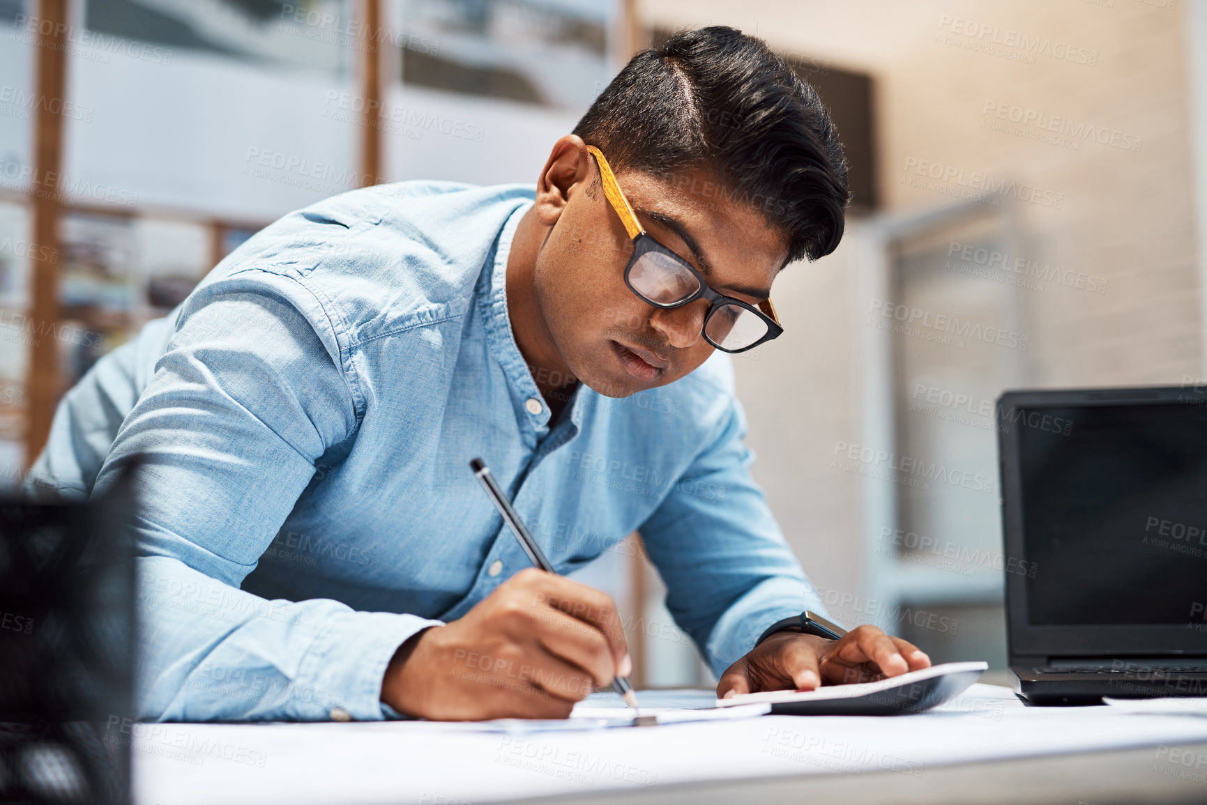 Buy stock photo Shot of a young architect using a calculator while drawing up a building plan