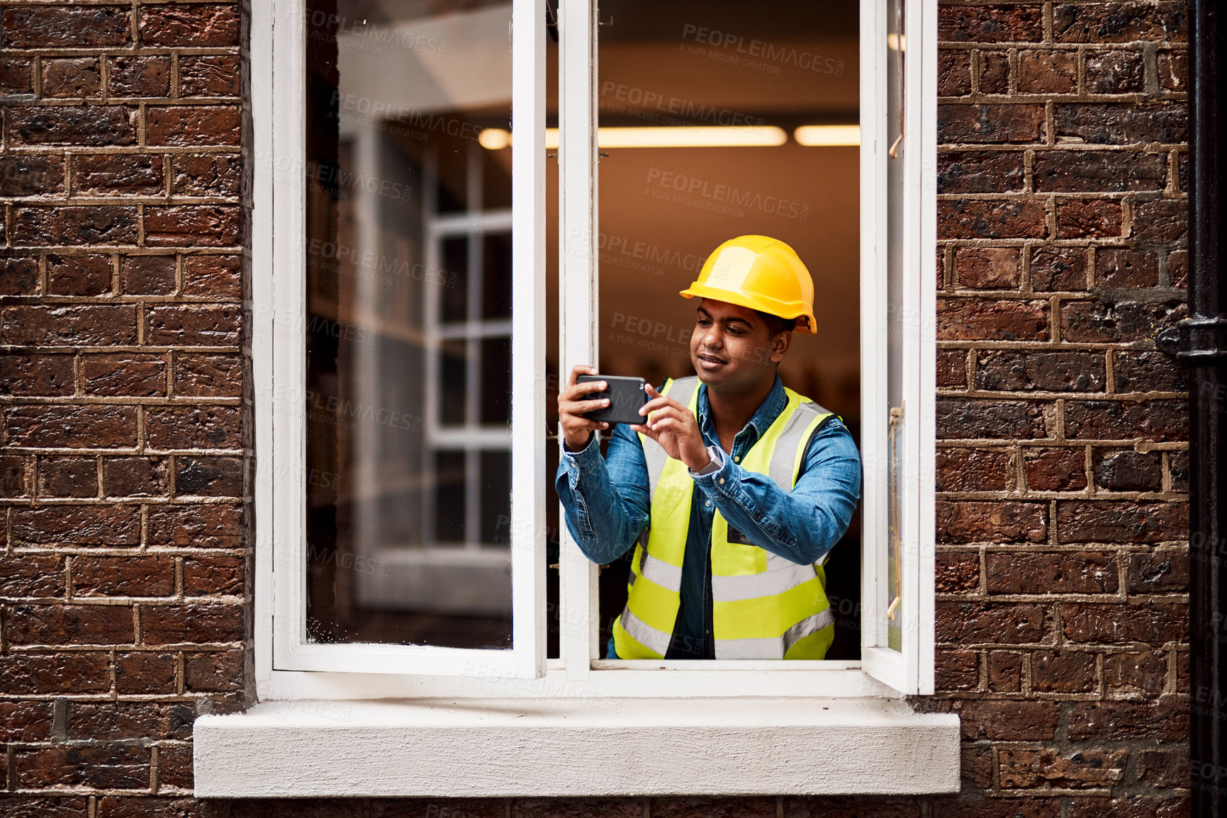 Buy stock photo Shot of a young engineer taking pictures while looking out the window of a construction site
