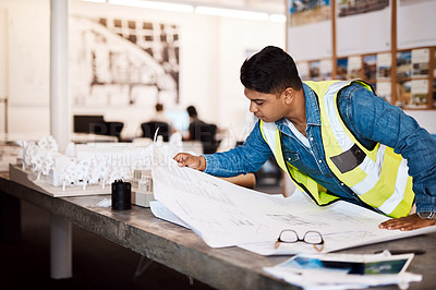 Buy stock photo Shot of a young architect looking at a blueprint in his office